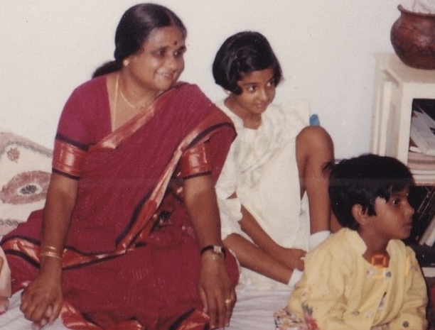 A picture of an adult sitting next to a child and both of them are smiling and looking at something a little further away. There's a younger child in front of them, not smiling.