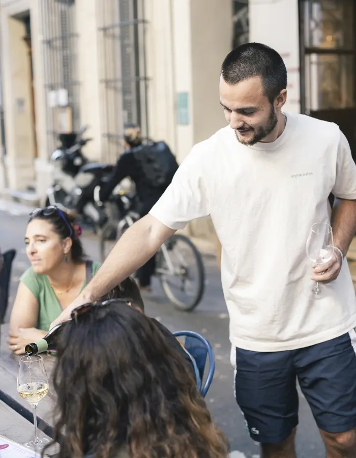 Serveur en terrasse du Marché des Argonautes boulevard Longchamp à Marseille en train de servir un verre de vin blanc à des clients.