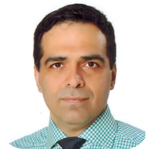 Portrait of a man with dark hair wearing a checkered shirt and dark tie against a white background.