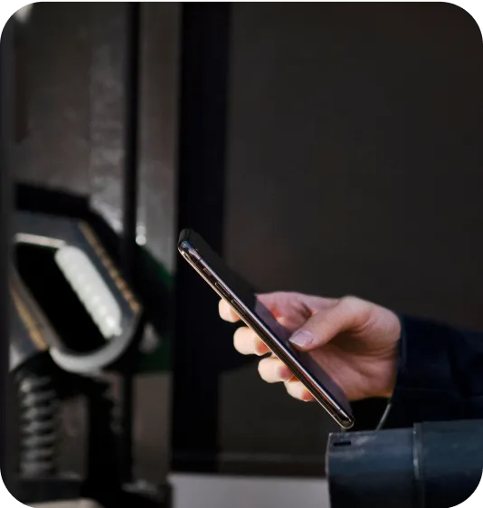 Hand holding a smartphone at a fuel pump station, indicating mobile payment or interaction.