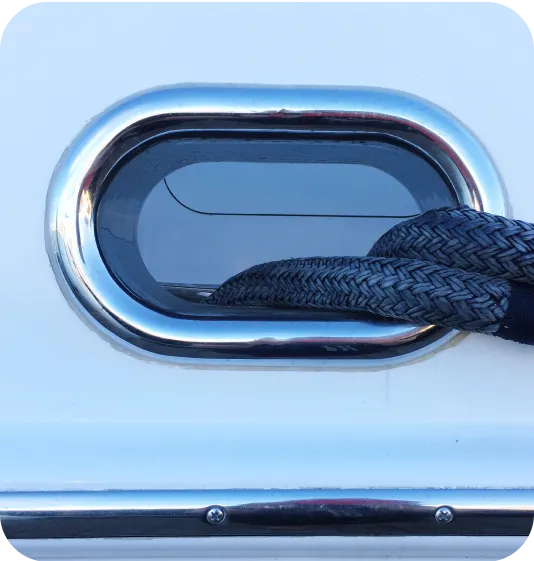 Close-up of a thick braided rope passing through a polished metal oval-shaped deck fitting on a white boat surface.