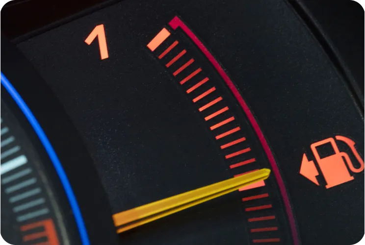 Car fuel gauge indicating almost empty with needle near the red zone and fuel pump icon.