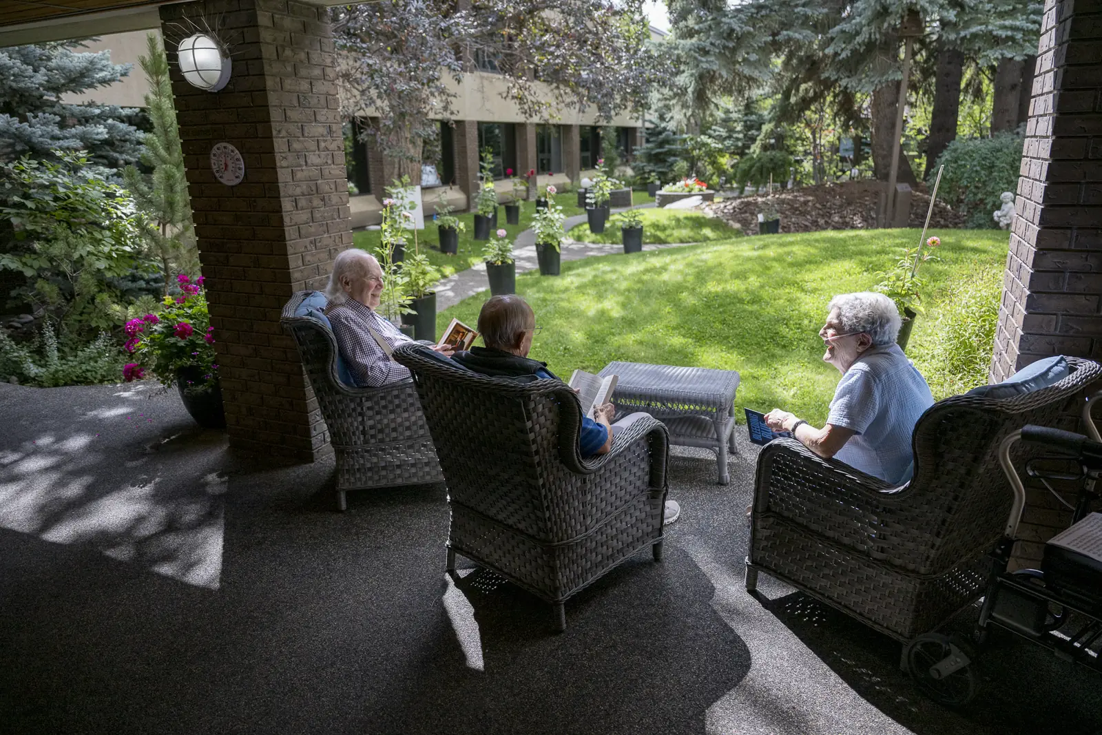 Three residents relax in wicker chairs on a covered patio, looking out over the courtyard lawn