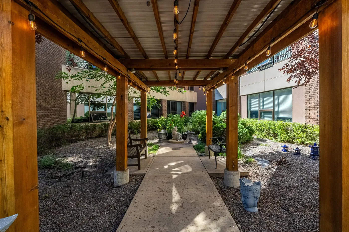 A wooden pergola strung with lights shades a garden path in a Trinity Lodge courtyard