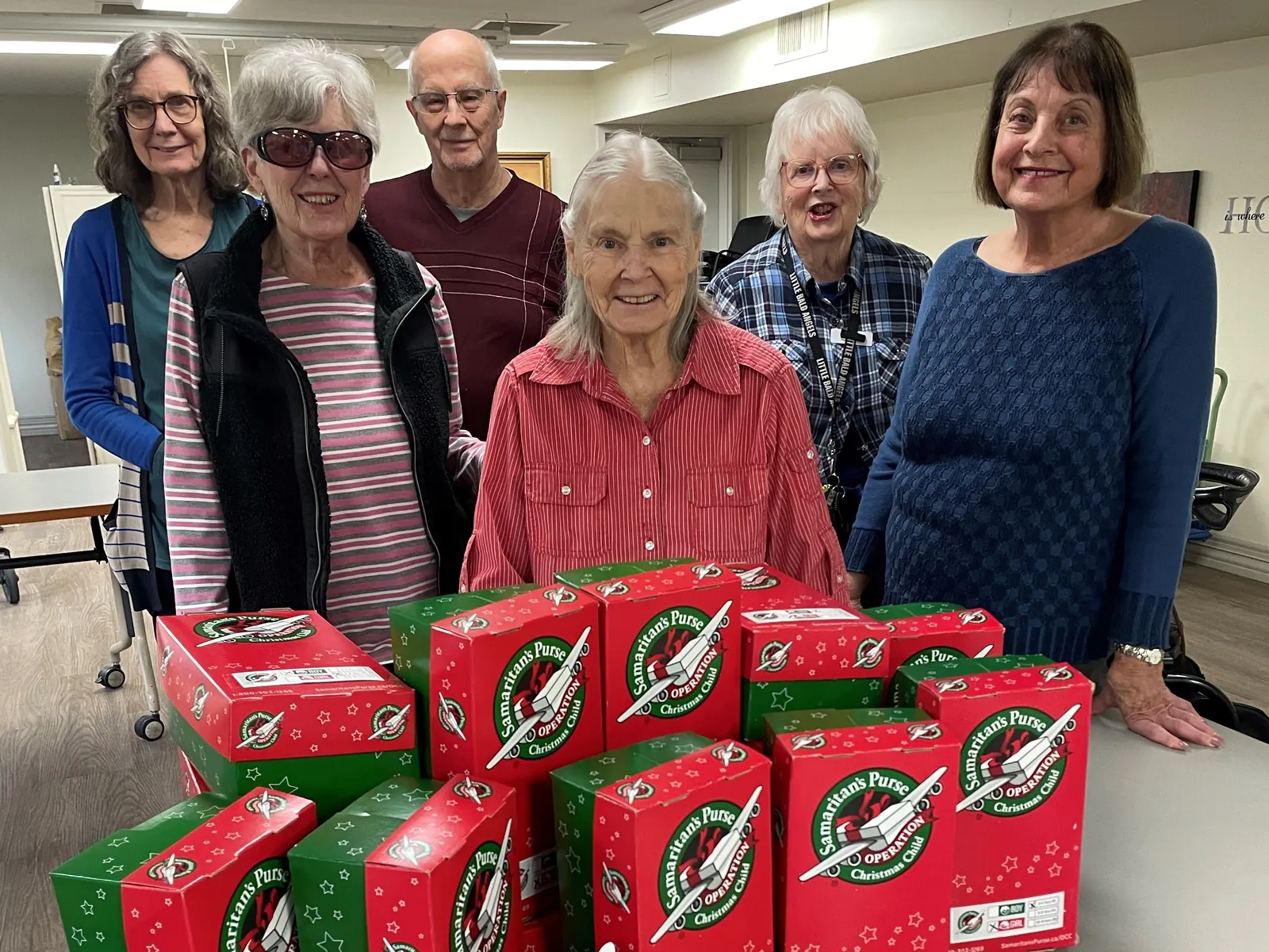 Six residents stand behind a table stacked with Operation Christmas Child shoeboxes