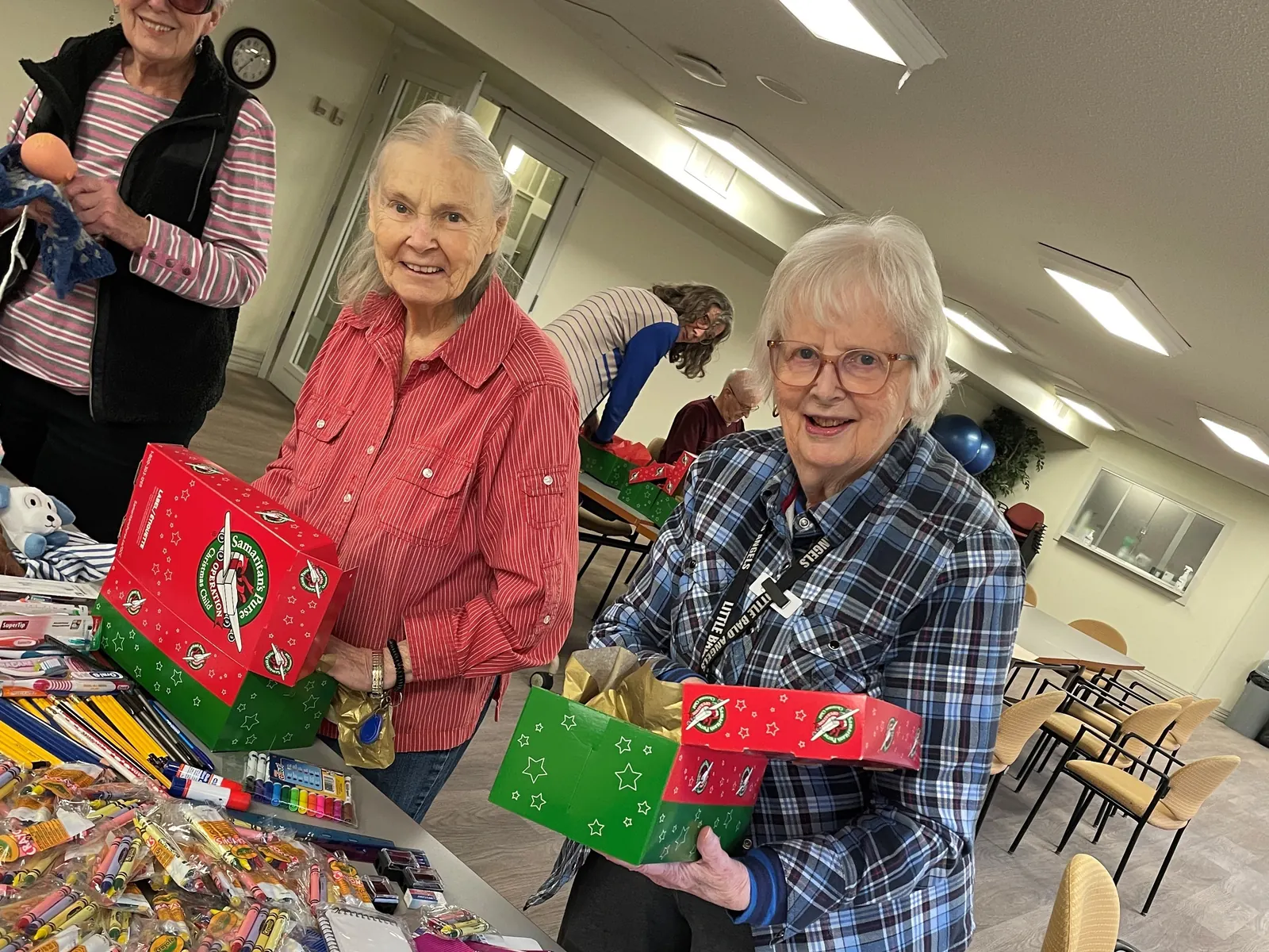 Two residents smile as they hold shoeboxes packed with gifts for Operation Christmas Child