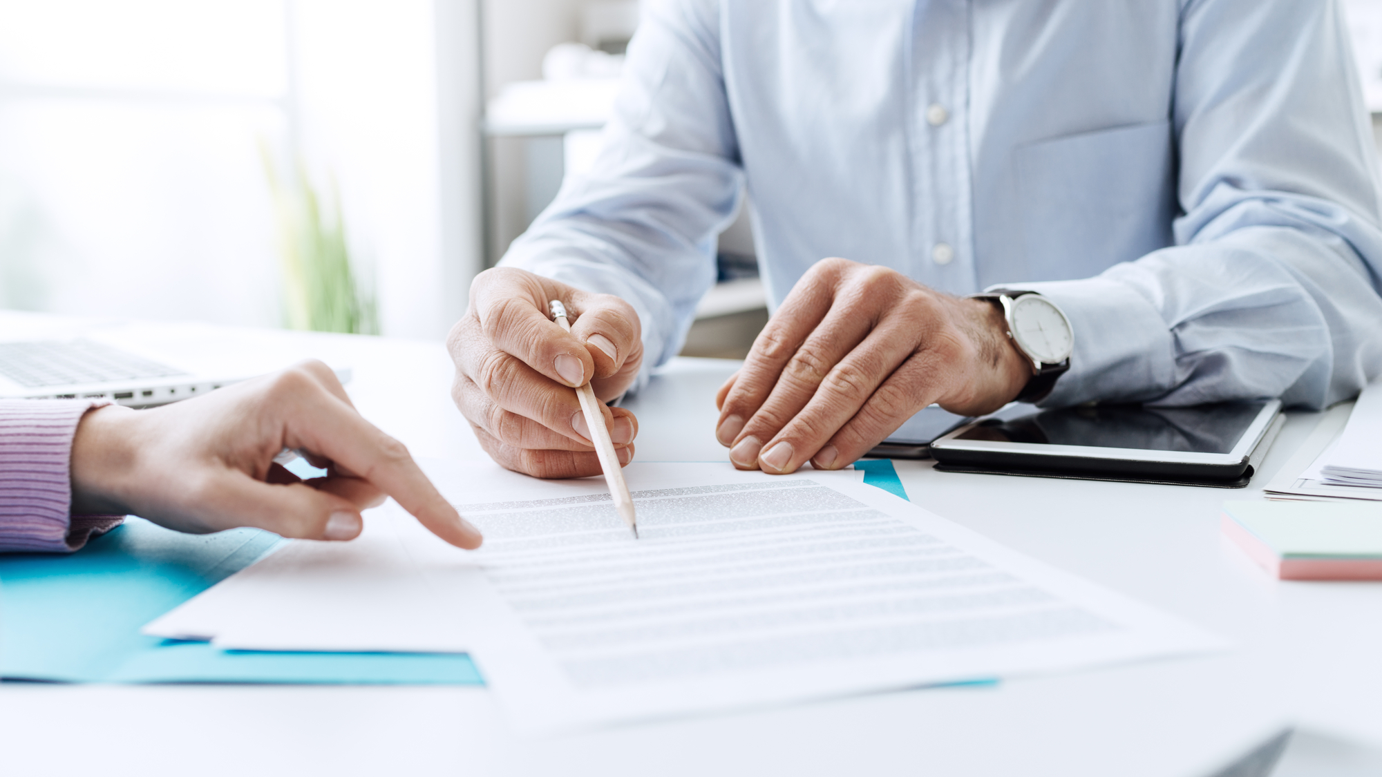 Two people sitting at a table with papers and a pen.