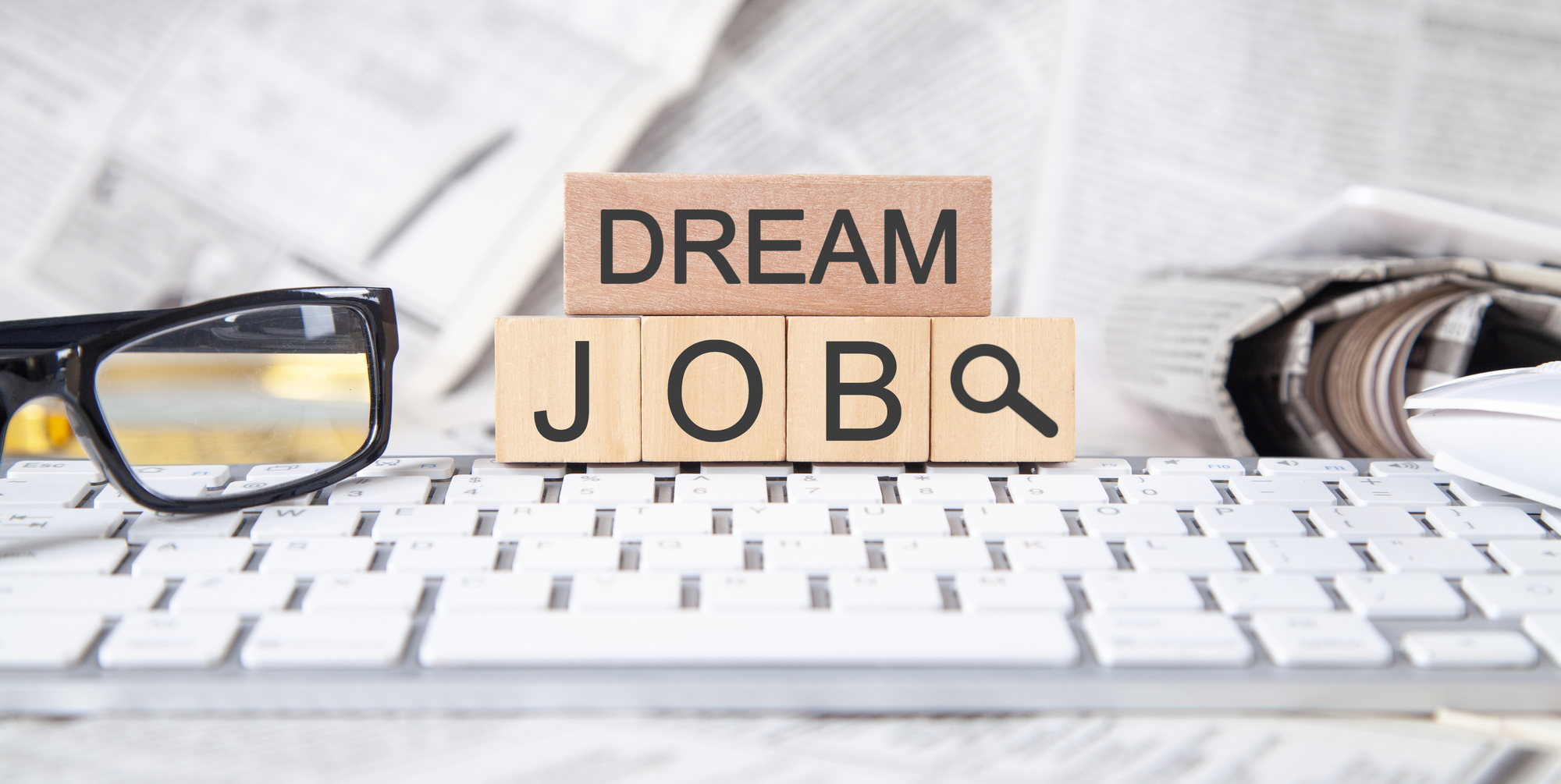 A wooden block that says dream job next to a pair of glasses.