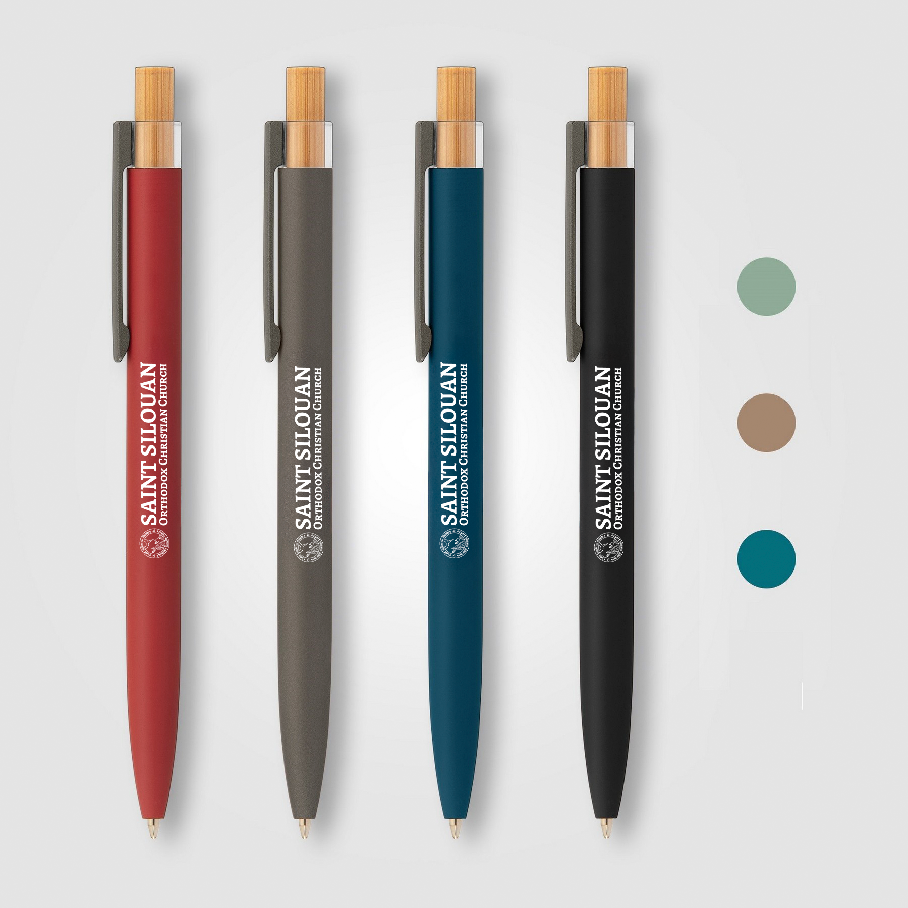 Four bamboo pens with clips, each in a different color—red, gray, blue, and black—with the text 'Saint Silouan Orthodox Christian Church' printed vertically in white on the barrel, alongside a circular logo.