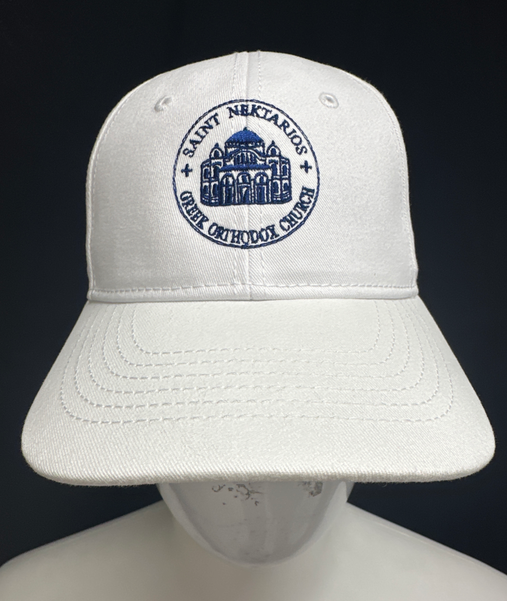 White baseball cap with blue embroidered emblem showing a church and the text 'Saint Nektarios Greek Orthodox Church' on the front.