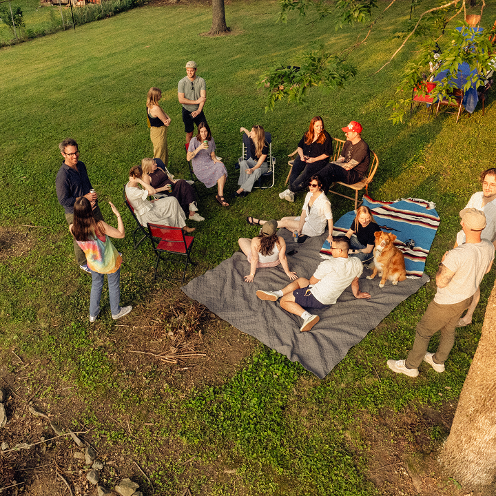 Aerial view of a large group of people enjoying a picnic and socializing in a grassy backyard setting.