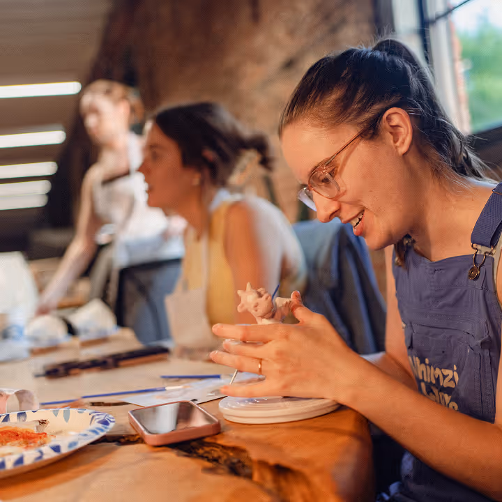 A woman sculpting a small figure at a wooden table during an art or pottery session.