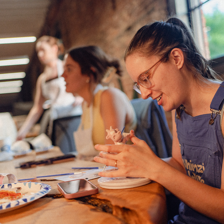 A woman sculpting a small figure at a wooden table during an art or pottery session.