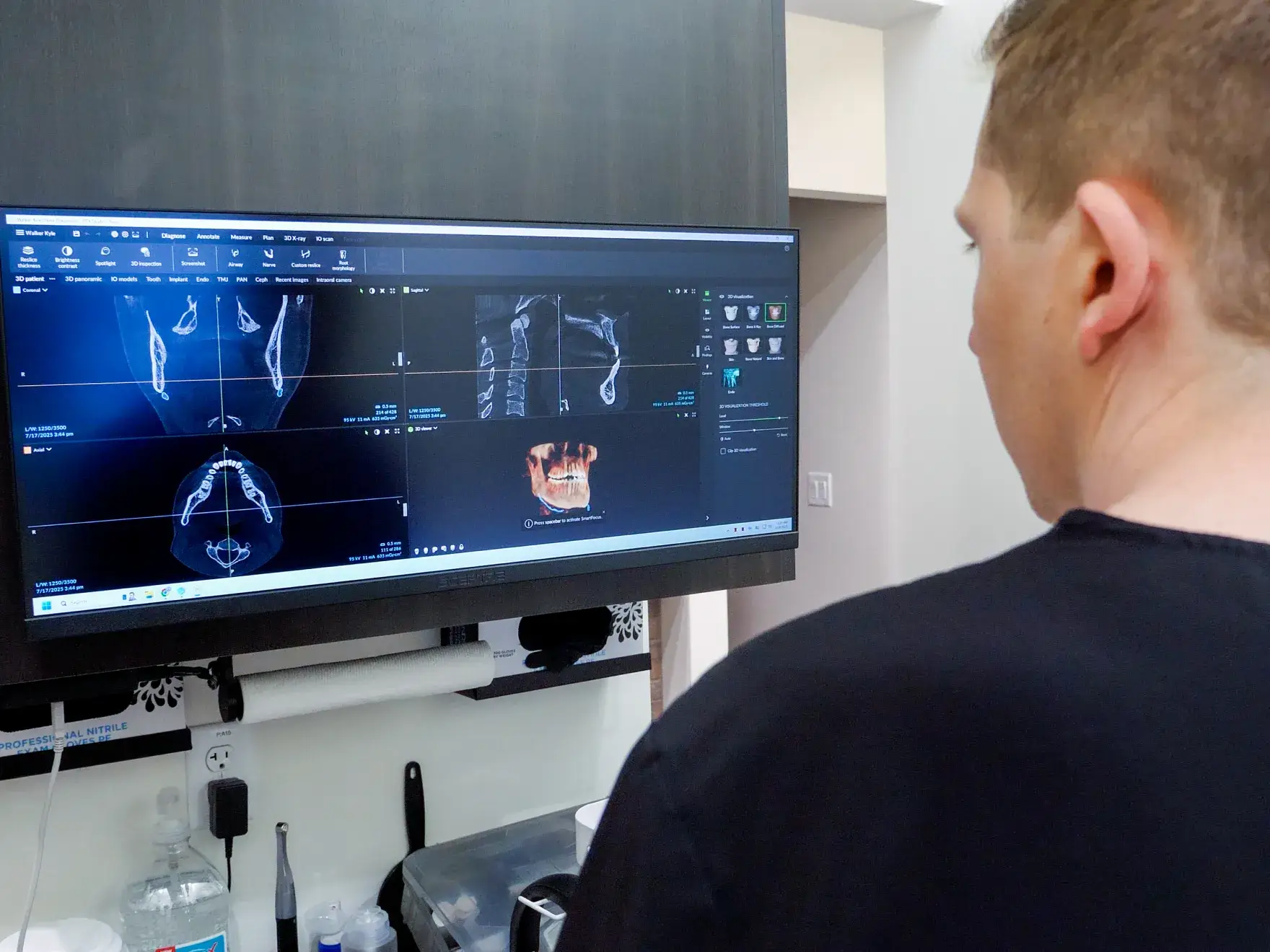 A dental professional in black scrubs uses equipment while examining a patient's teeth with digital imaging.
