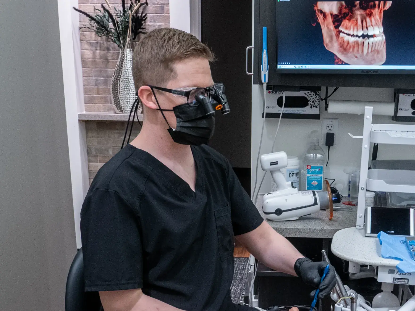 Two people wearing black scrubs stand with arms crossed, smiling in front of a brick wall.