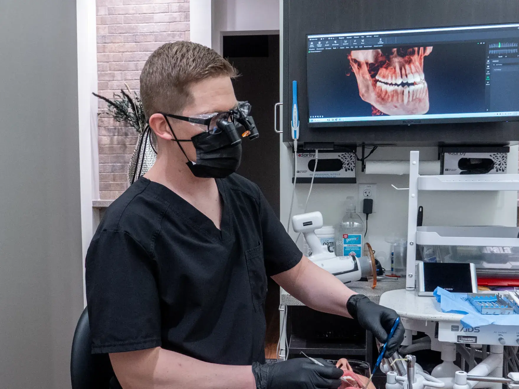 A woman in a dental chair holds a mirror while a dentist points to her teeth.