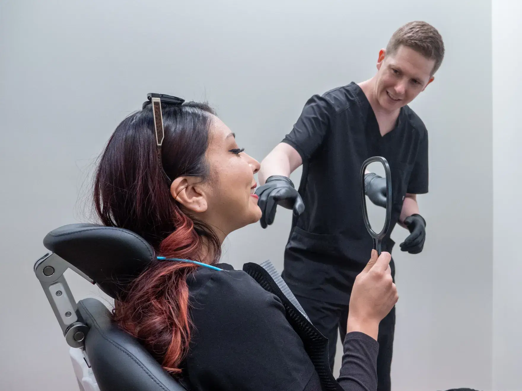 Two people in black scrubs smiling and talking to each other inside an office setting.