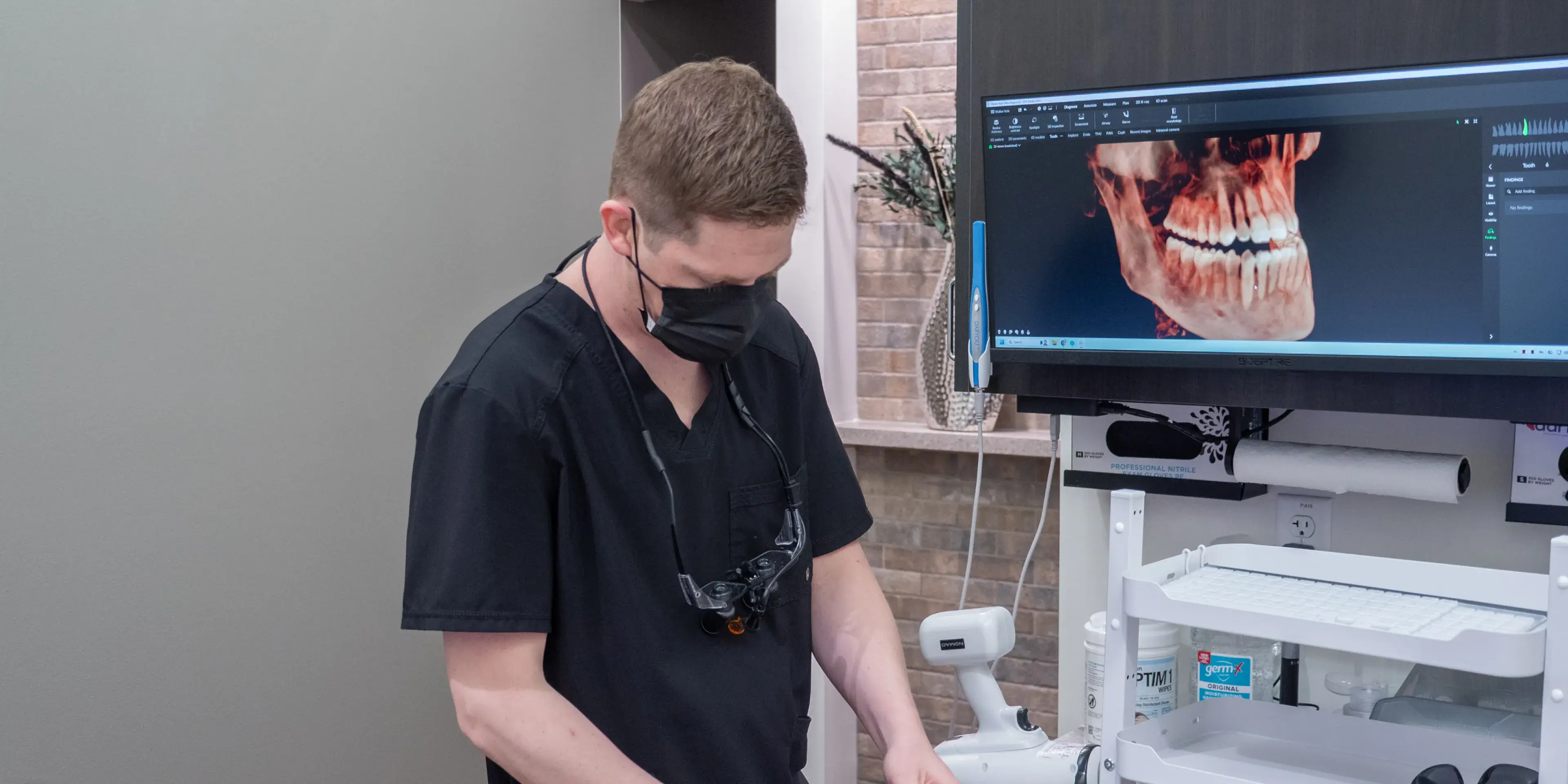 A dentist explains a dental X-ray to a patient using a large monitor in the office.