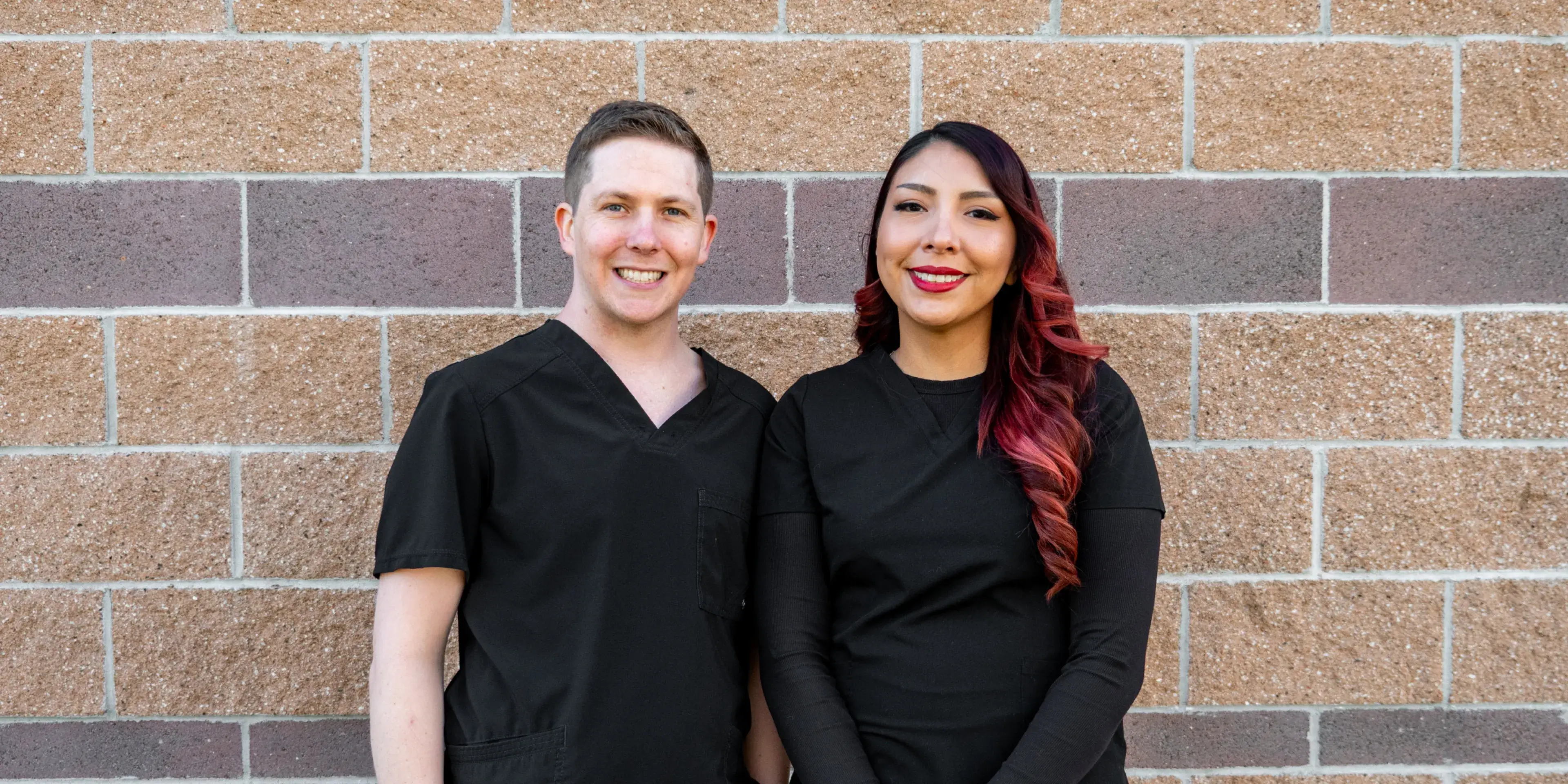 A man and a woman in black uniforms work at a computer in an office.