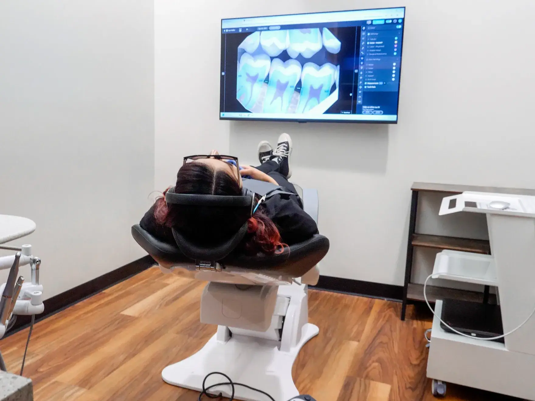 A dentist wearing magnifying glasses works on a patient while wearing a face mask and gloves.