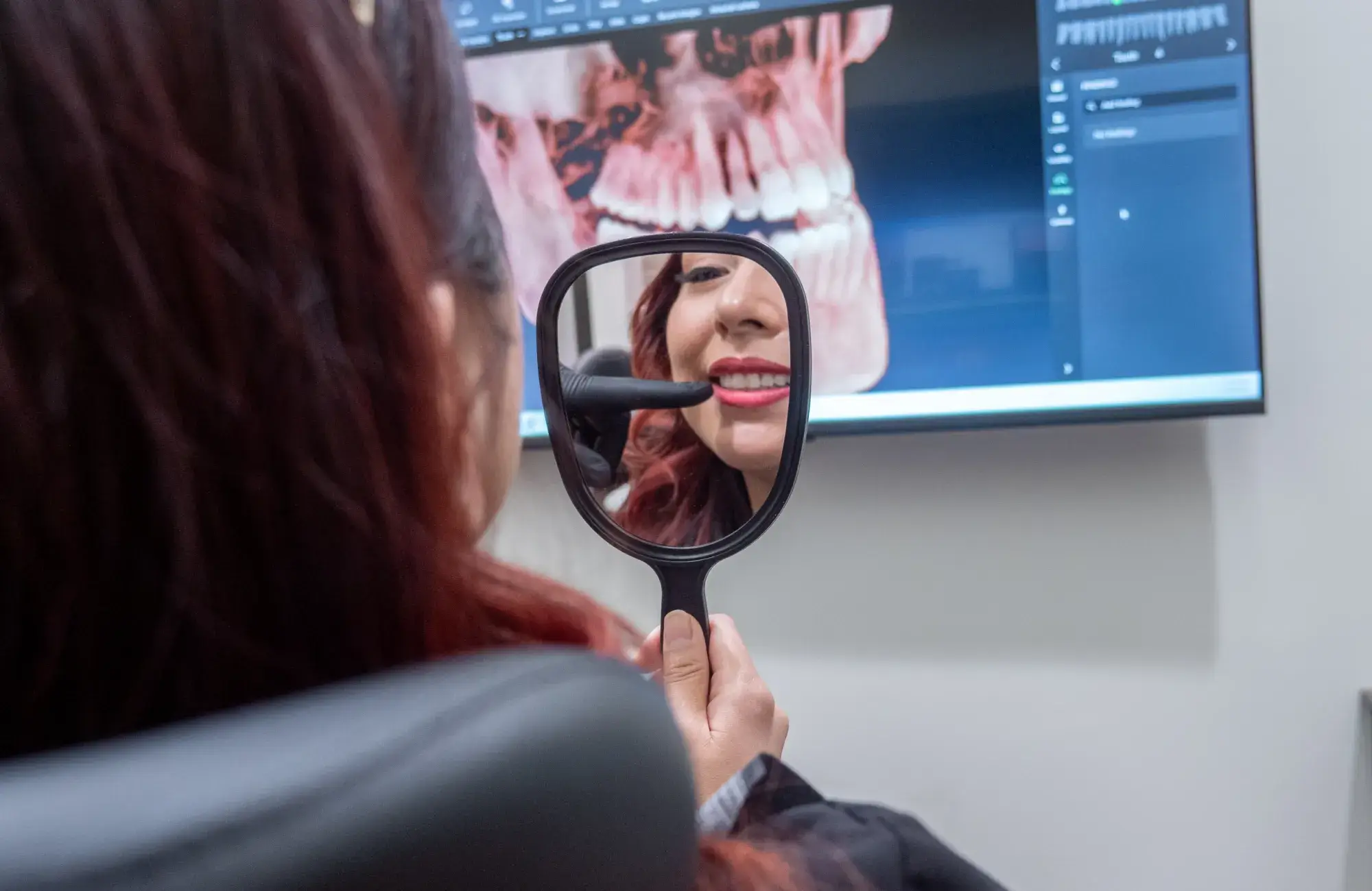 A dentist wearing a mask examines dental x-rays on a computer screen in an office.