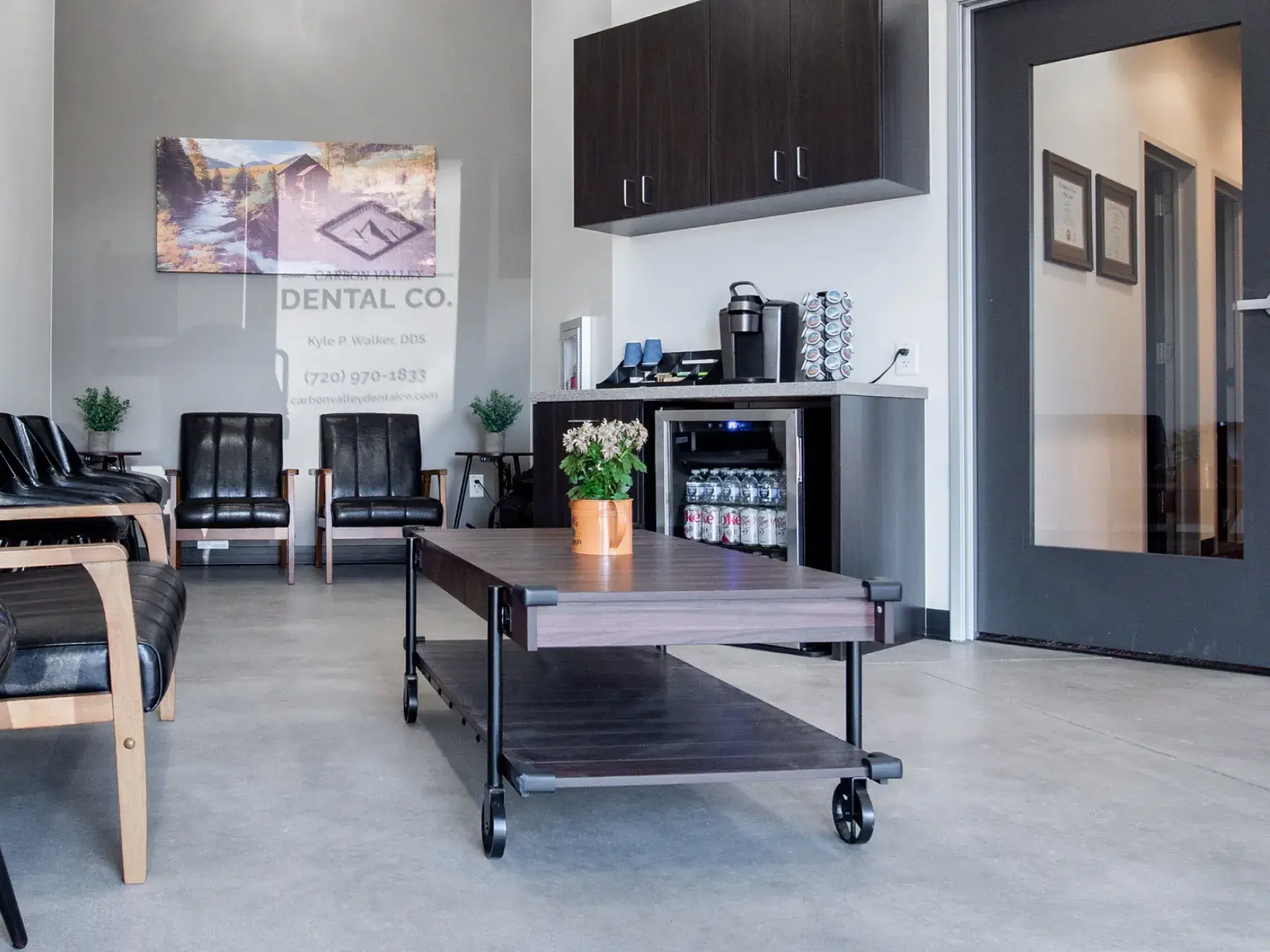 A dentist smiles and points at a dental image on a monitor while explaining to a patient.