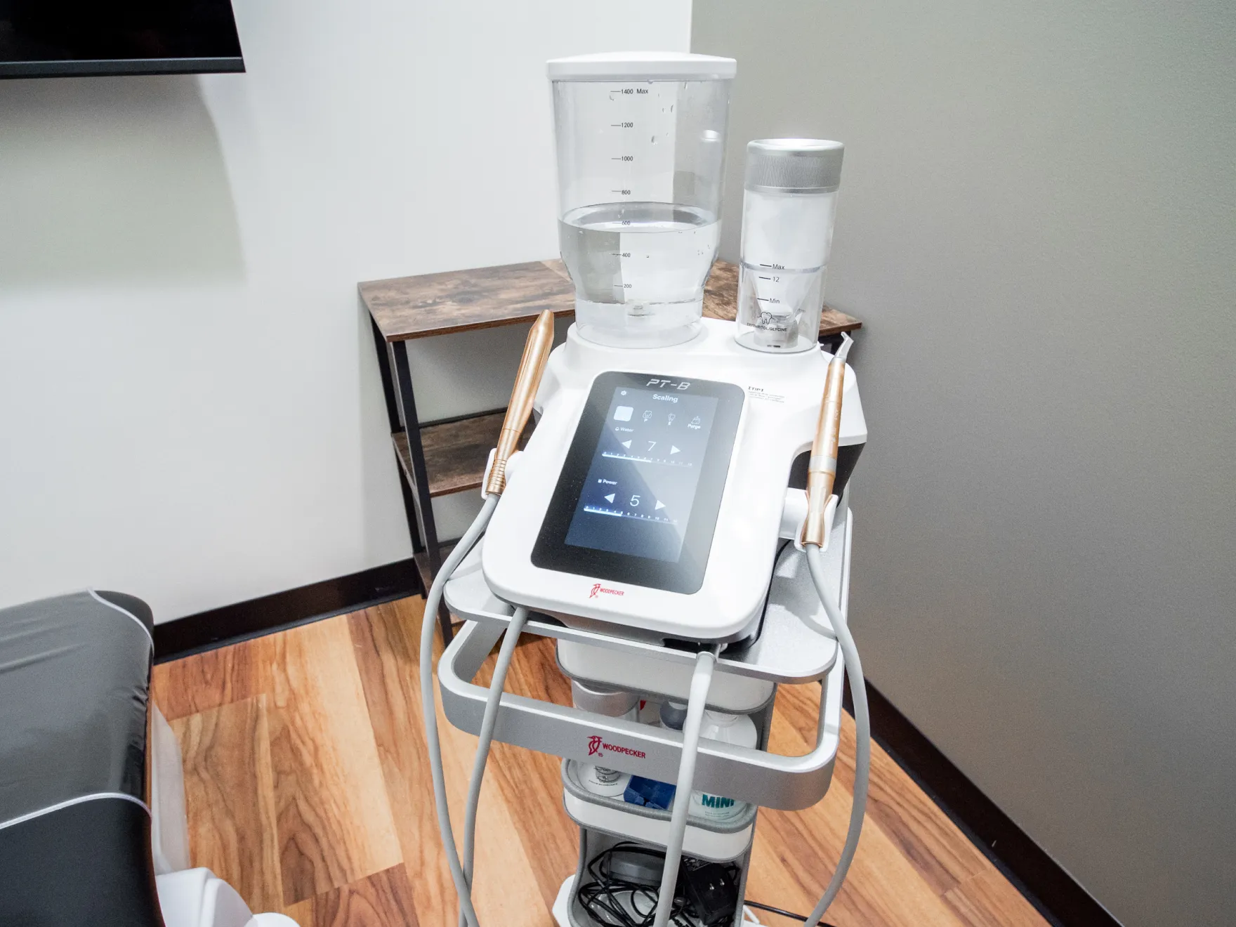 A medical device with a touchscreen and two attached hoses sits in a room with wooden floors.