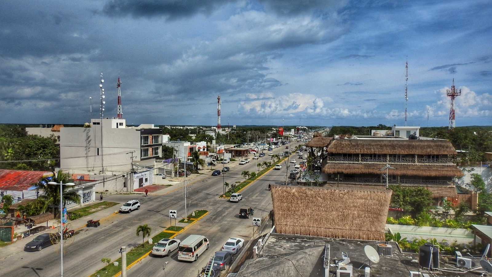 Avenida Tulum seen from above, traffic on the main avenue with palapa-roofed buildings alongside