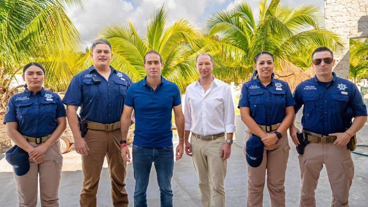 Four Tulum Policia Ejecutiva officers in blue uniforms standing with two officials under palms in the hotel zone