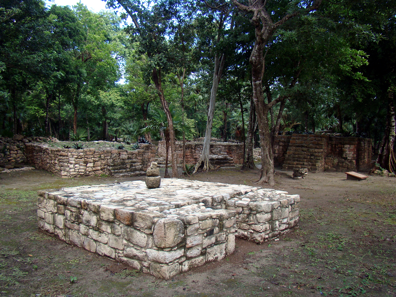 A low stone altar in a cleared plaza at Xel-Ha, ringed by trees and ruined walls