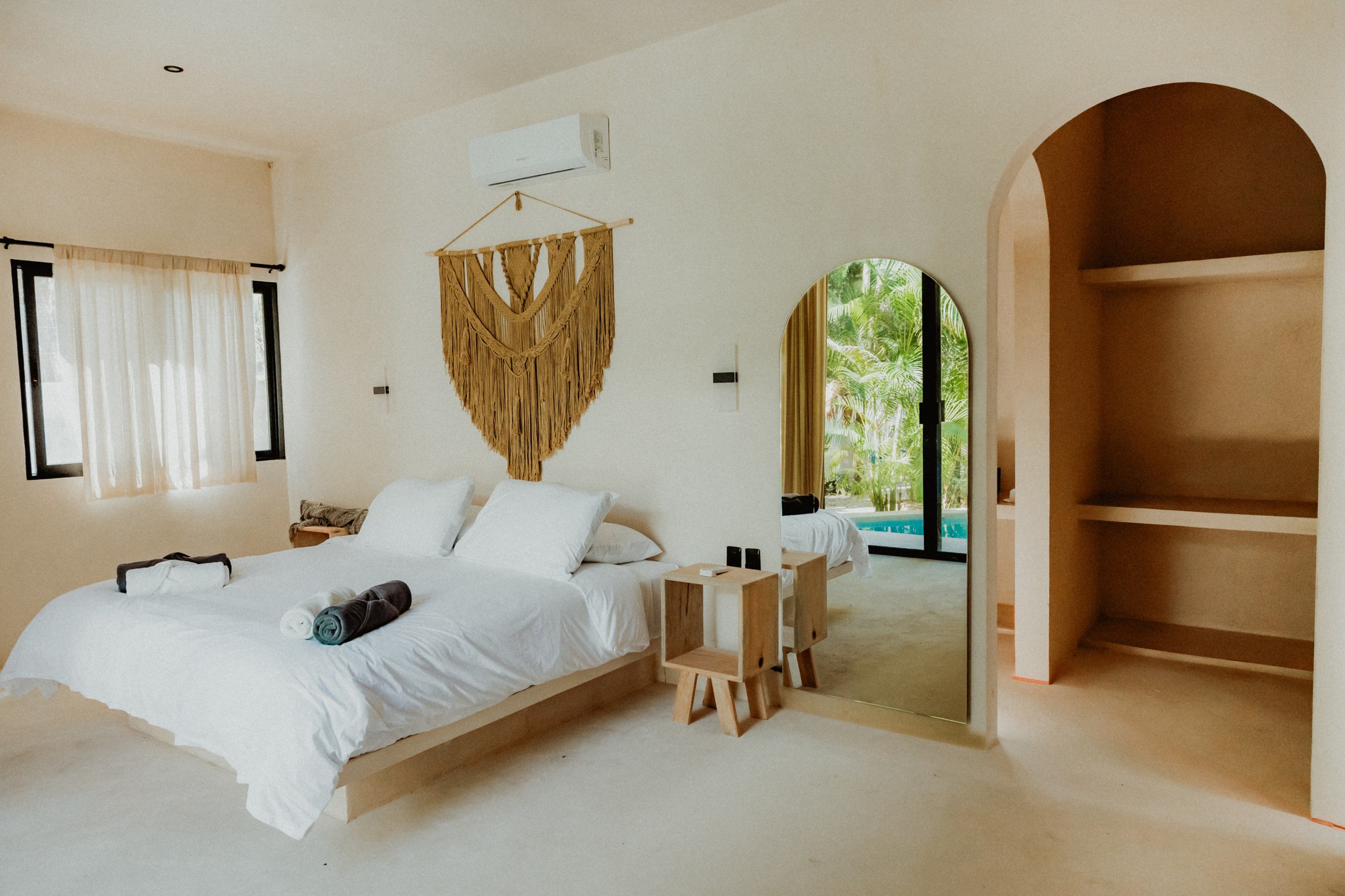 Bedroom with macrame wall hanging, arched shelving niche and a doorway through to the pool