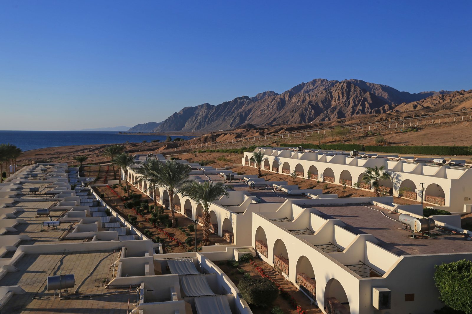 A low rise resort strung along a desert coastline with bare mountains behind