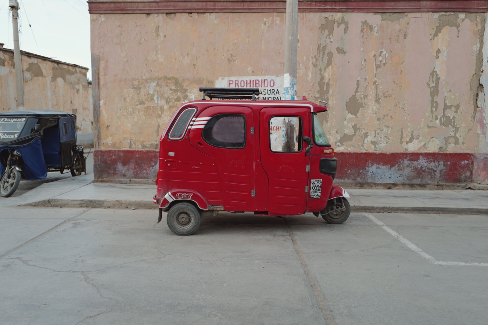 A red three wheeled mototaxi parked against a weathered wall in Mexico