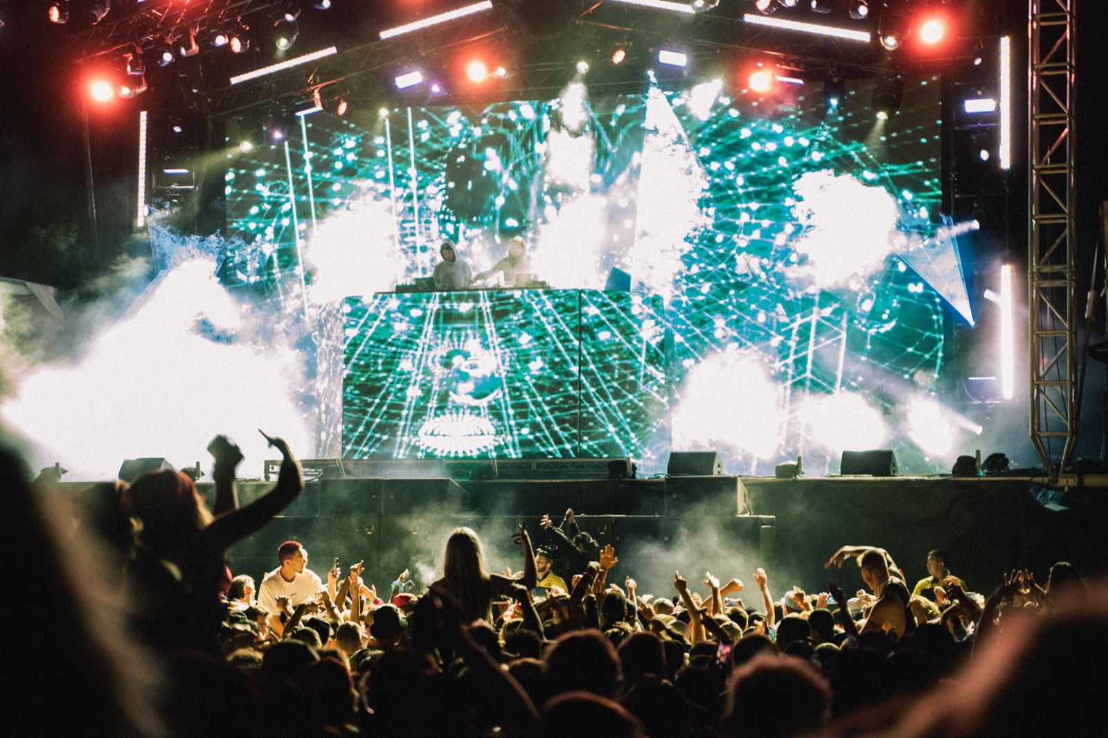 A crowd in front of an open air festival stage lit in green and white at night