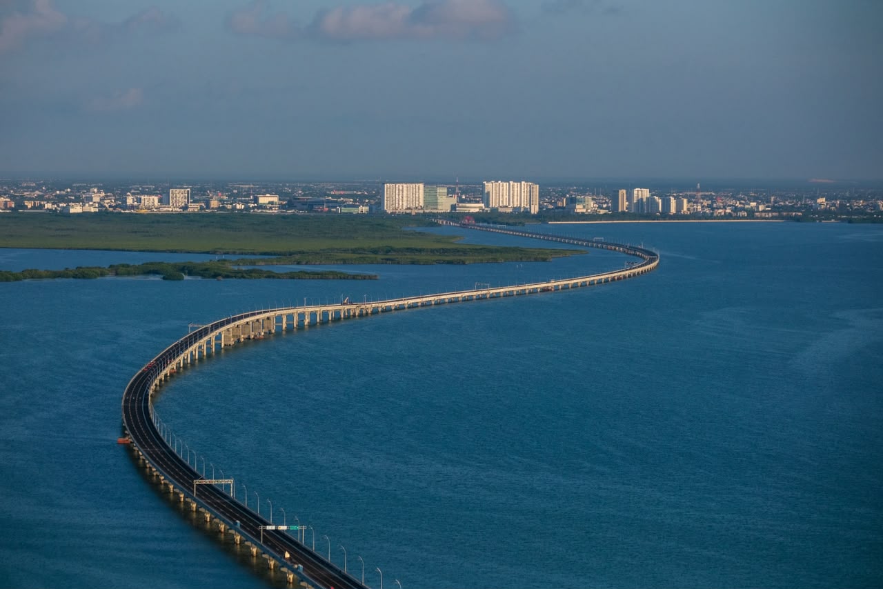 Aerial view of the Nichupté bridge curving across the blue lagoon toward the Cancún skyline