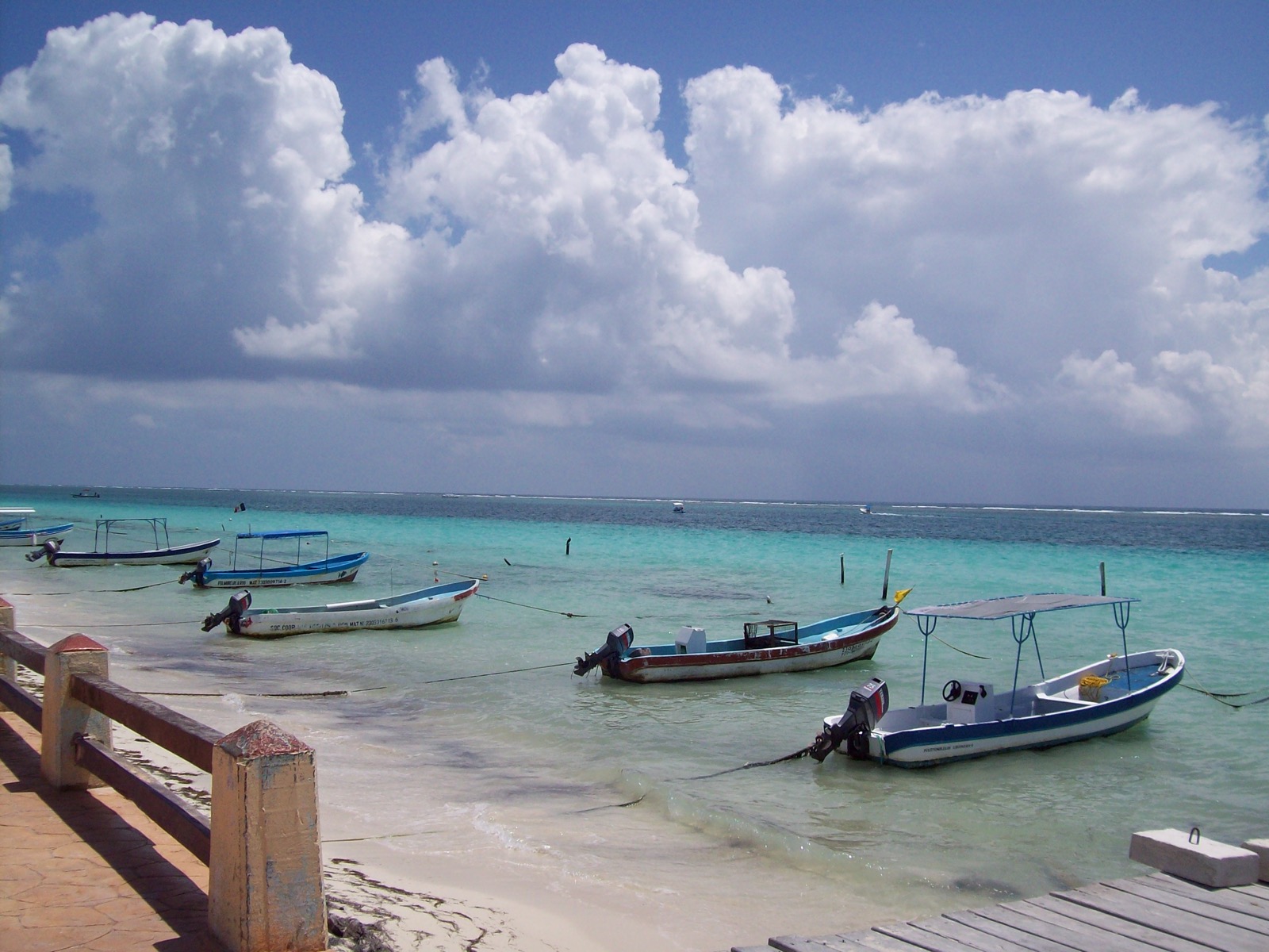 Blue and white fishing boats registered to Puerto Morelos moored in shallow water at the edge of the beach under a cloudy sky