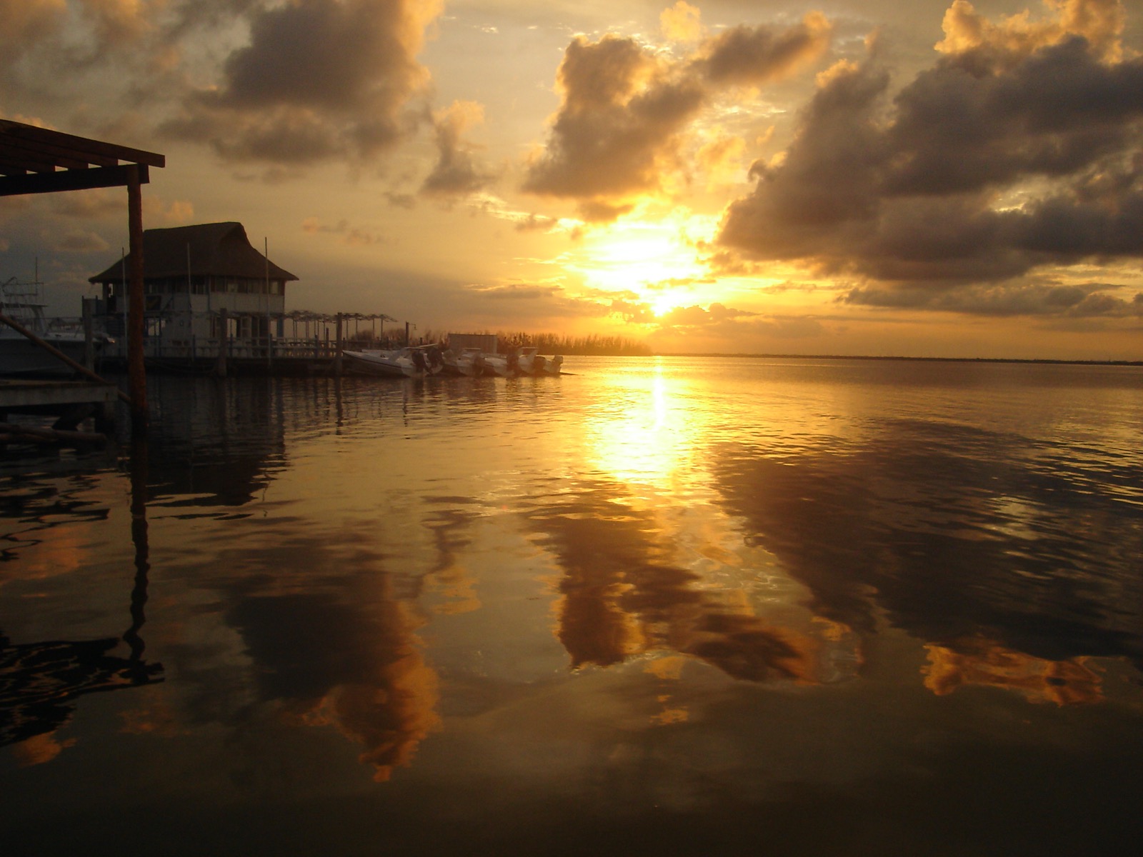 Sunset over the calm Nichupté lagoon, with small launches moored at a dock beside a palapa roofed building