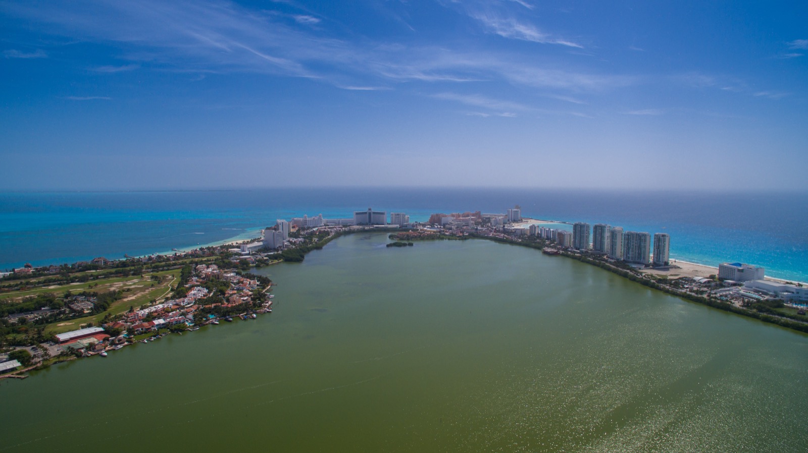Aerial view over the Nichupté lagoon toward Cancún's hotel zone, a narrow strip of hotels and towers between the lagoon and the Caribbean