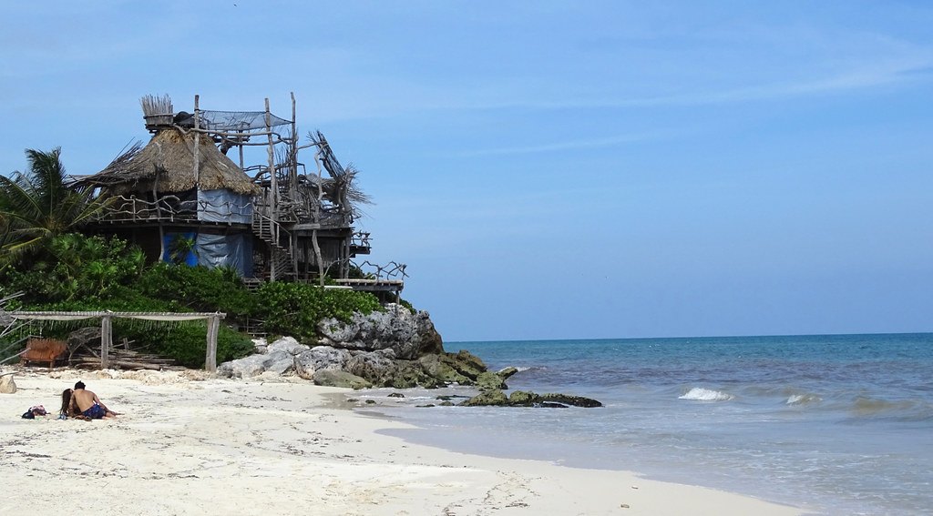 A quiet stretch of white sand and clear water at Playa Tulum, below a palapa and timber lookout
