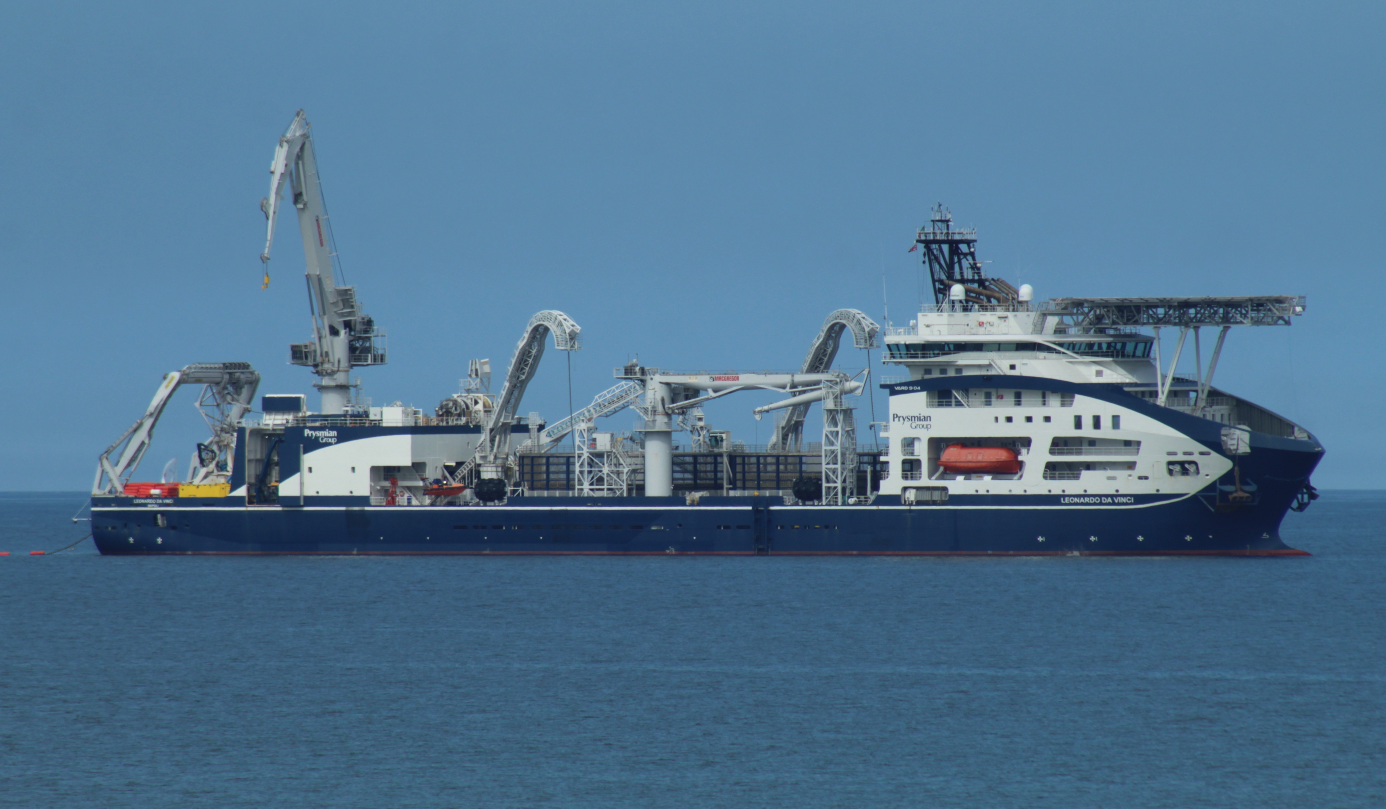 A cable-laying ship with cranes and a cable carousel on deck, at sea