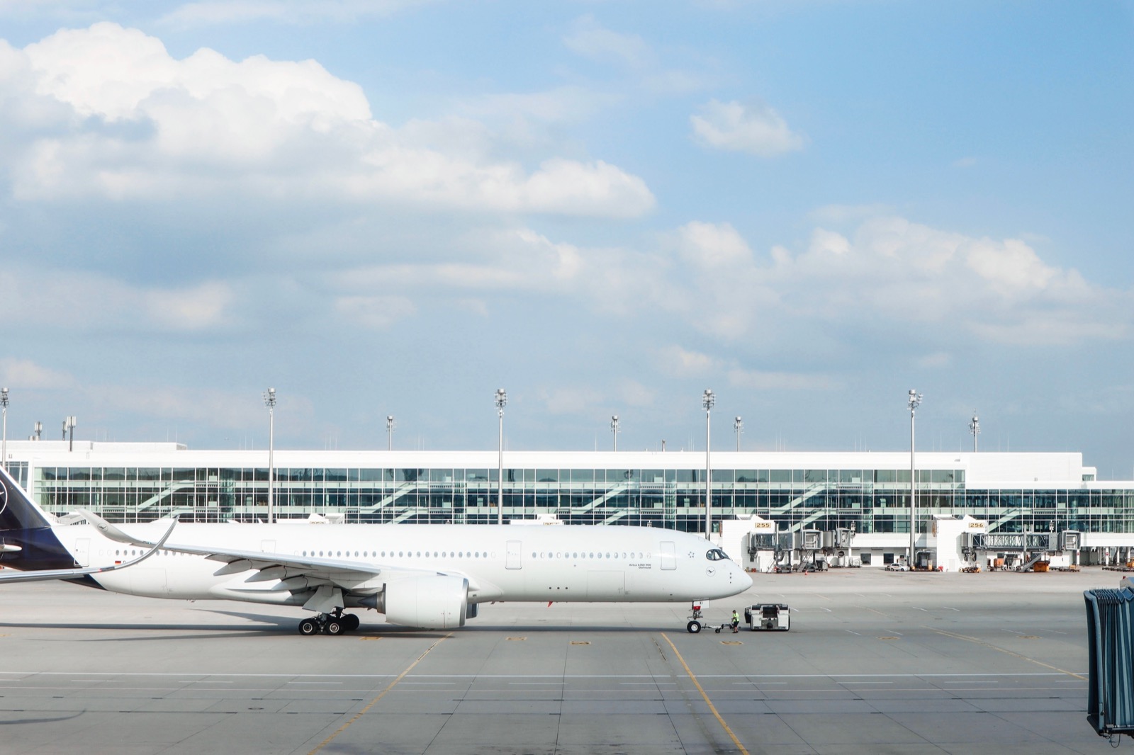 A wide-body passenger jet parked on an airport apron in front of a long glass terminal under a partly cloudy sky
