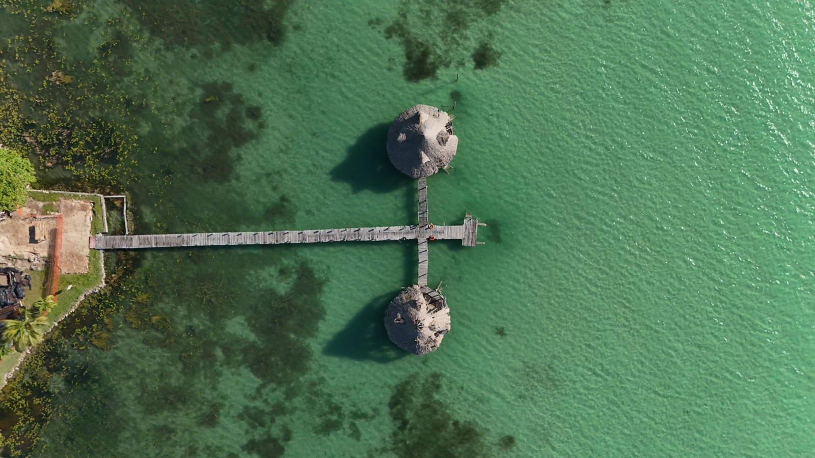 Aerial view of a wooden pier with palapa platforms over the turquoise Bacalar lagoon