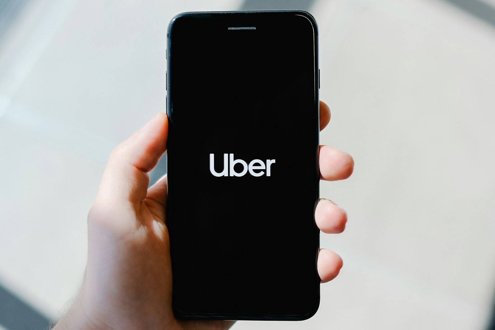 A hand holding a smartphone showing the Uber logo on its start screen.
