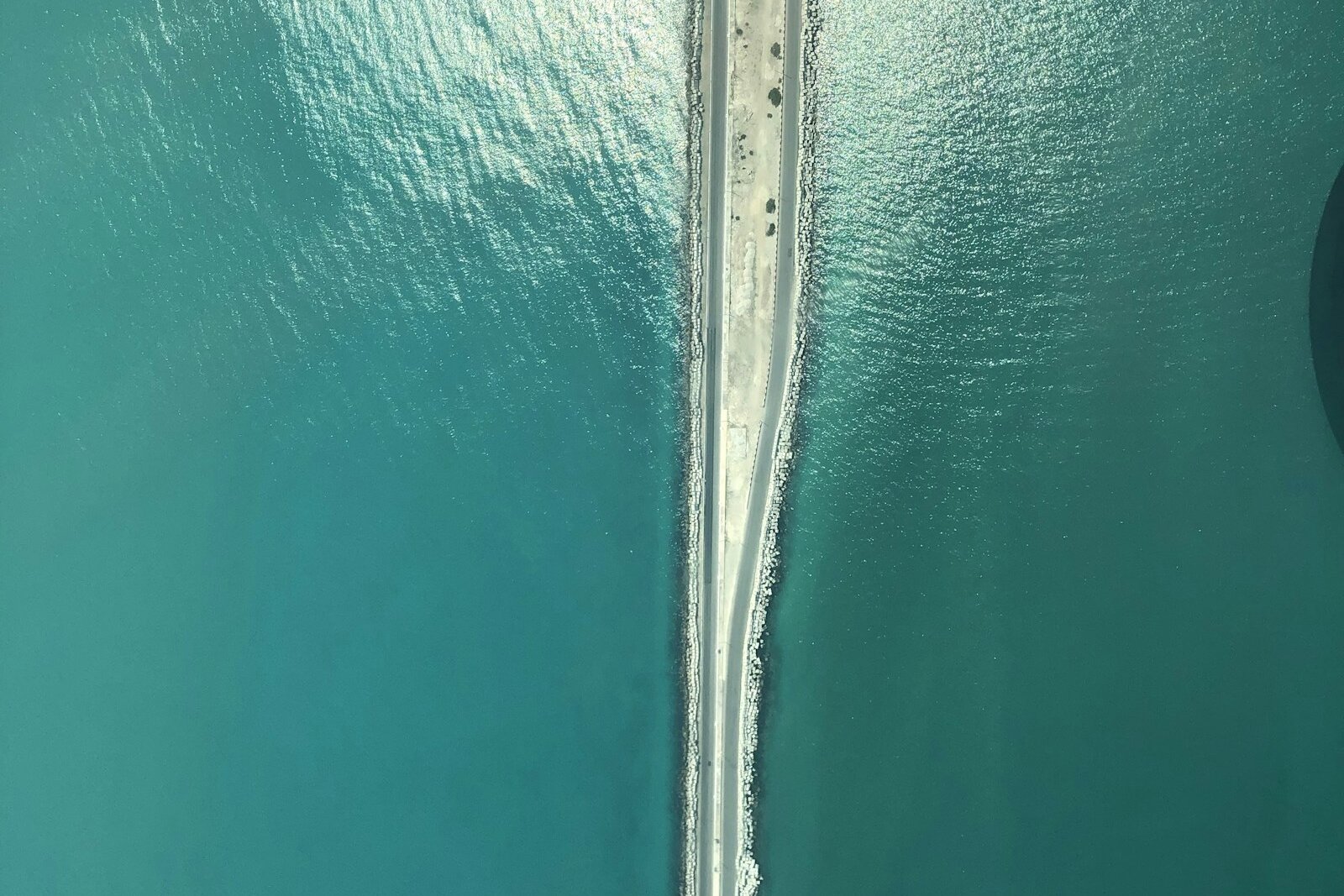 An aerial view of a long, narrow road on a causeway running straight across turquoise sea.