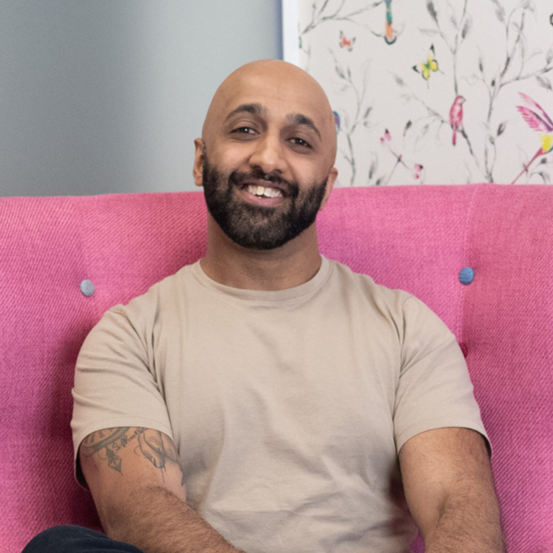 Man sat in pink chair with a neutral t shirt and a beard