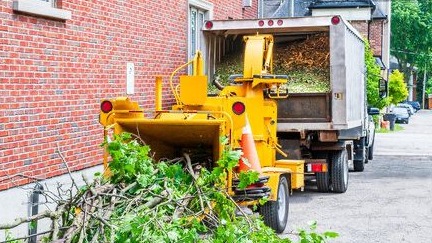 A specialised machine chipping branches into mulch. Mulch is being fed into the back of a tipper.
