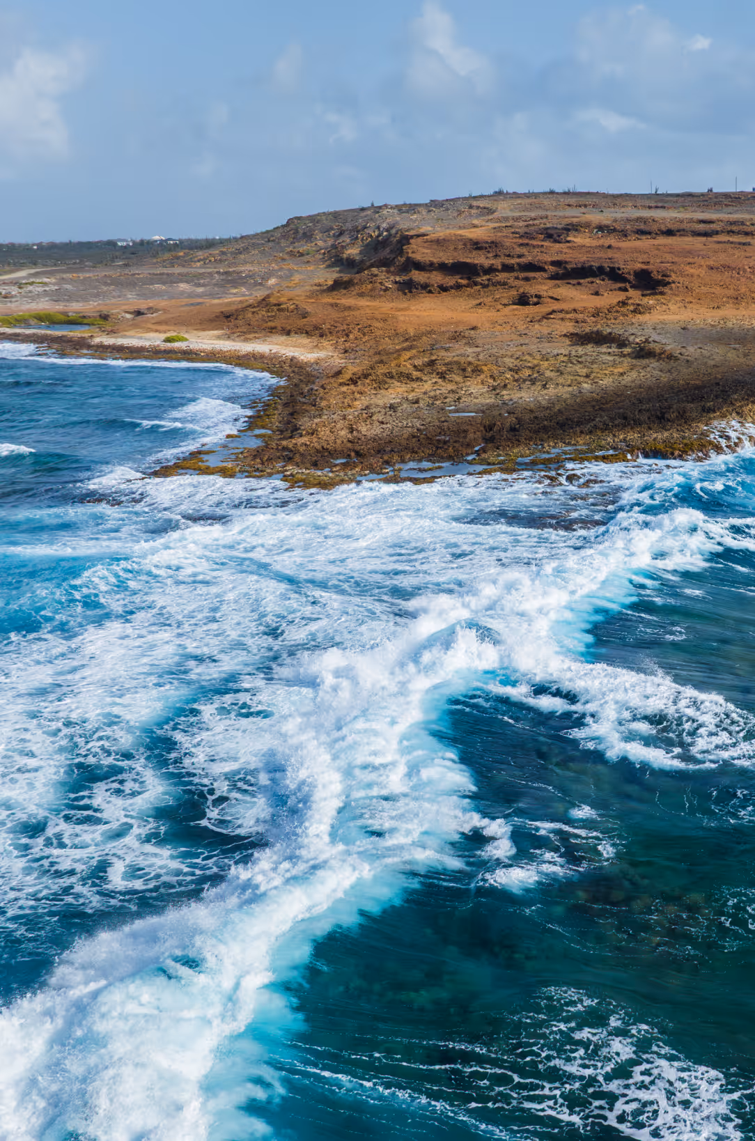 Waves crashing against a rocky coastline with rugged brown cliffs under a cloudy sky.