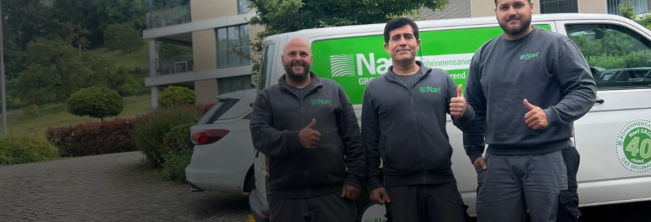 Three men standing in front of a van giving thumbs up.