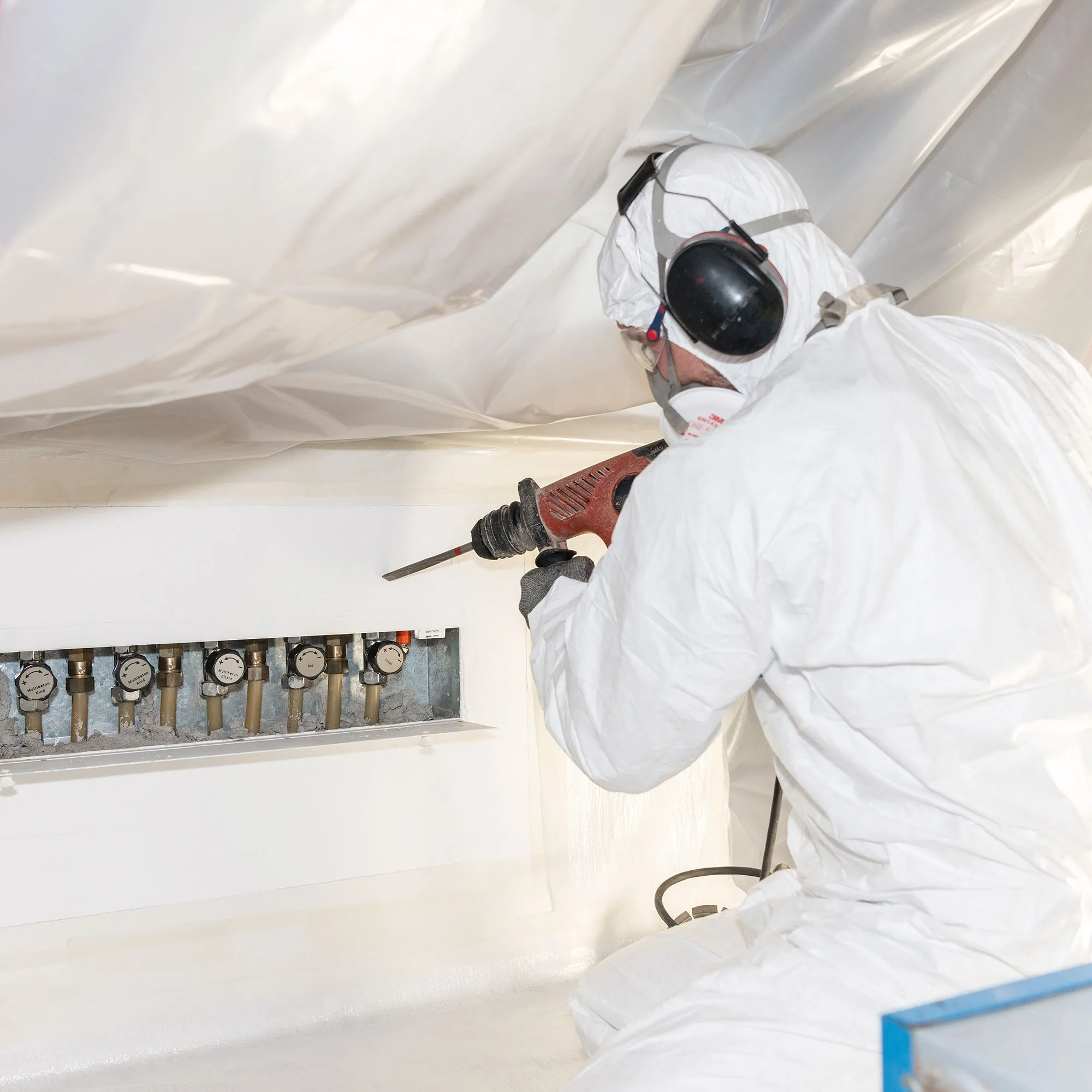 A man in a white coverall spray painting a wall.