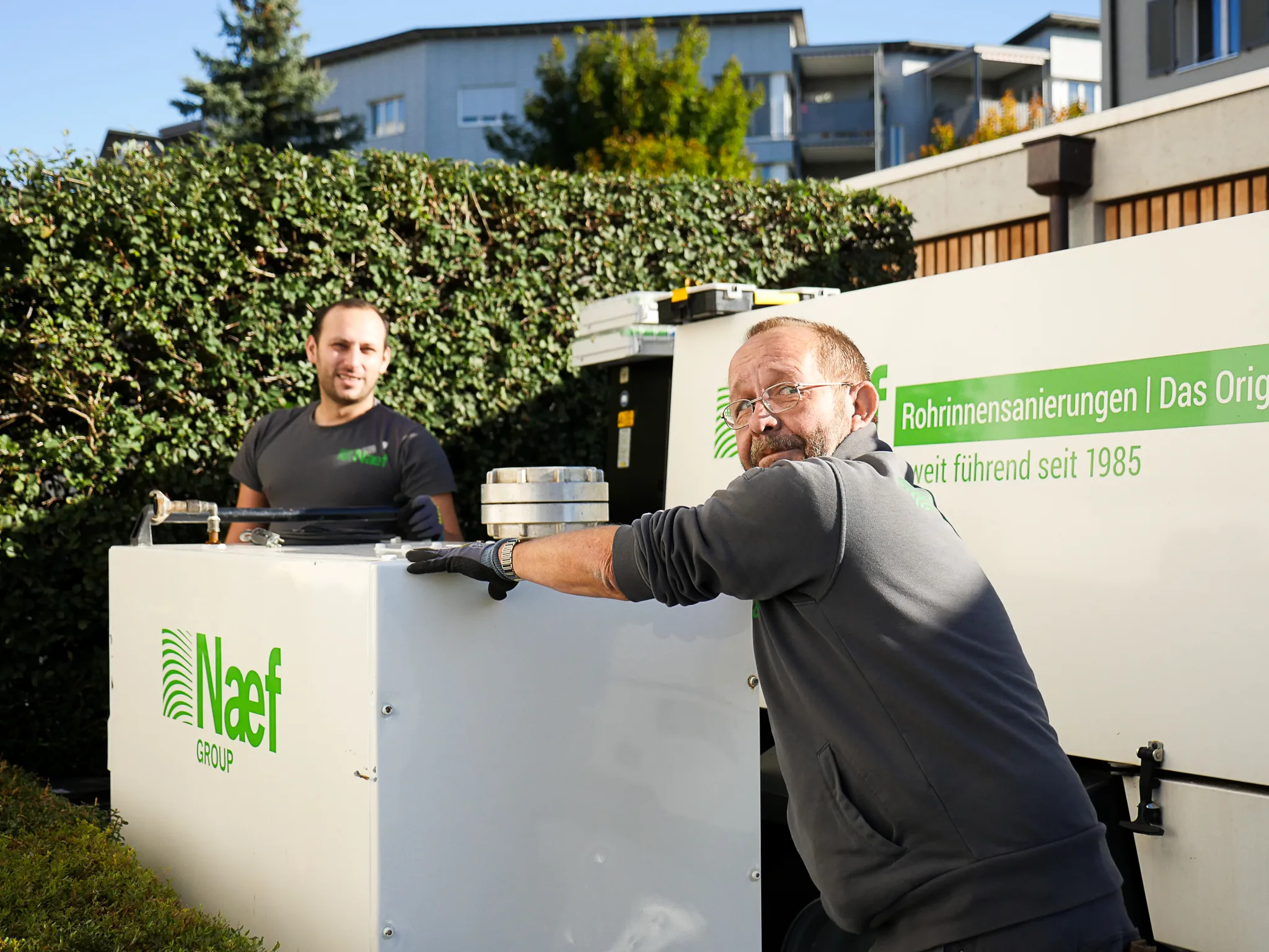 Two men standing next to a white refrigerator.